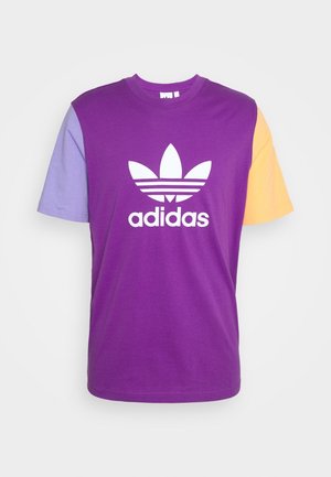 Fioletowa bawełniana koszulka z krótkimi rękawami, z lawendowymi i żółtymi akcentami. Na środku biała logo Adidas z trzema paskami poniżej.