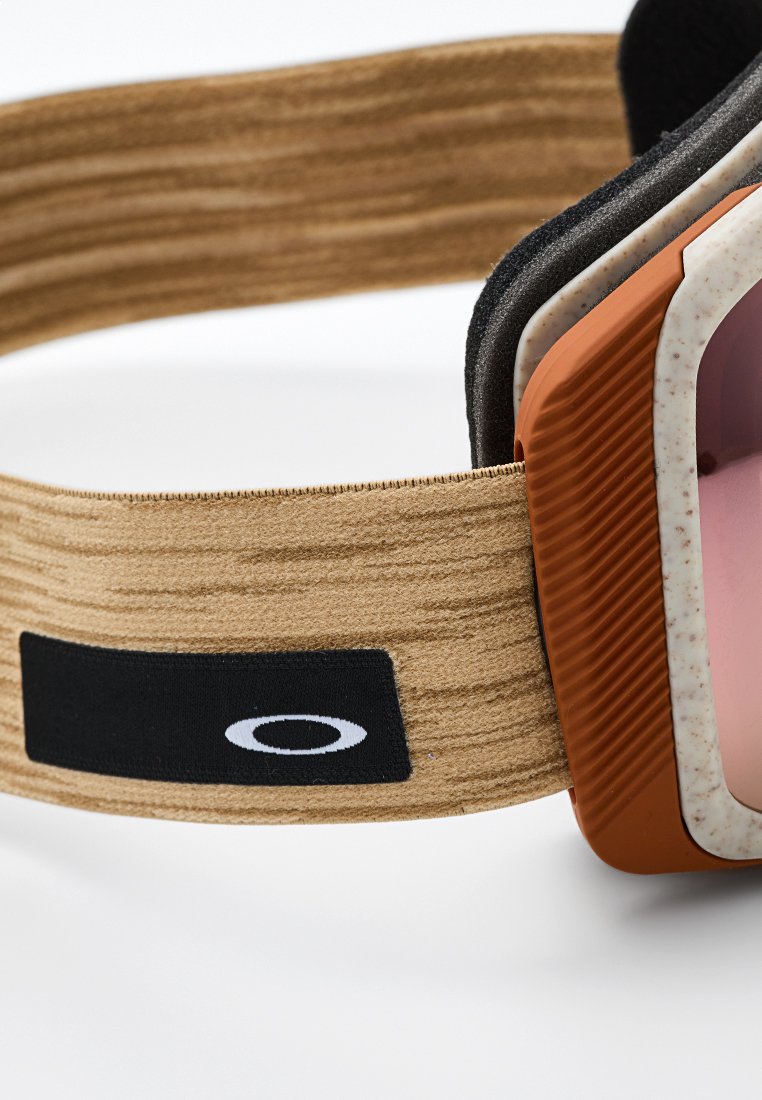 Skibrille mit einem strap aus braunem Holzmaserung, orangefarbenen Elementen und rosa getönten Gläsern. Auffälliges schwarzes Logo-Patch am Band.