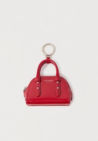 Czerwona mini torebka z lakierowanej skóry jako brelok z srebrnym pierścieniem i logo „kate spade new york” na białym tle.