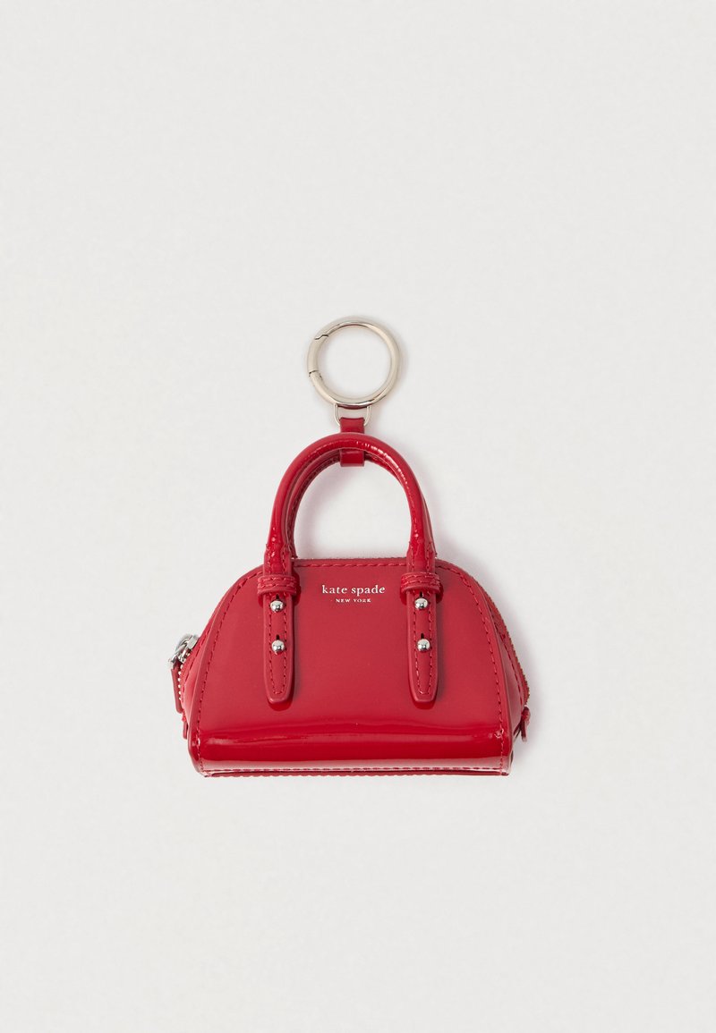 Czerwona mini torebka z lakierowanej skóry jako brelok z srebrnym pierścieniem i logo „kate spade new york” na białym tle.