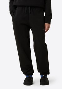 Pantalones deportivos negros con un ajuste relajado, que cuentan con una cintura elástica con cordón. Detalle de logotipo notable en el muslo izquierdo. Textura de tela suave.