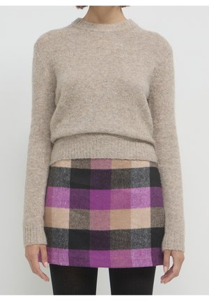 Pull en maille beige à manches longues associé à une mini-jupe à carreaux violette, noire, beige et marron et des collants noirs.