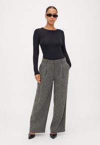 Melna ilga piedurkne bluze, apvienota ar augsto jostu pelēkām plašām houndstooth biksēm; modele valkā melnus norādītus zābakus un saulesbrilles.