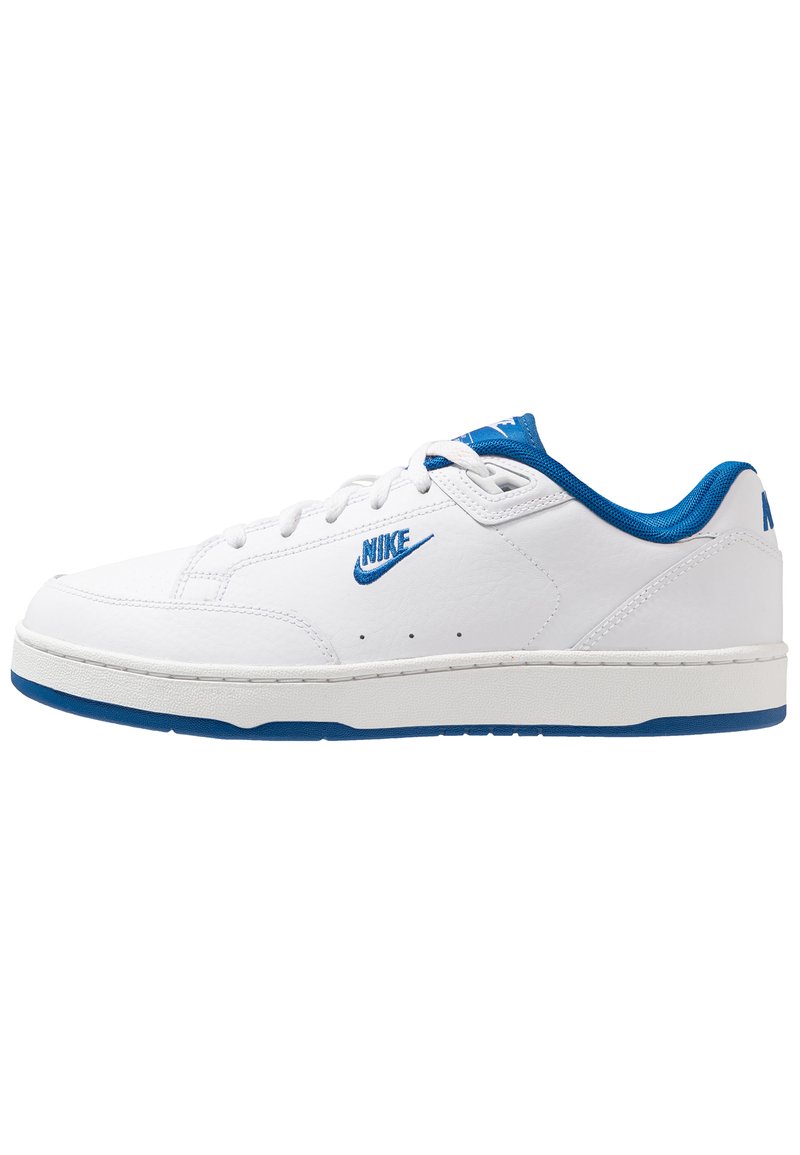 Fehér bőr Nike sportcipők kék akcentusokkal. Lapos talppal, perforált részletekkel az oldalán és kék fűzőkkel rendelkezik.