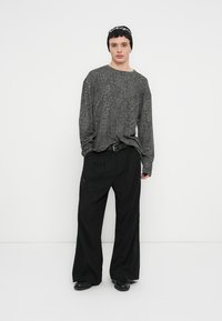 Chemise à manches longues à imprimé léopard gris associée à un pantalon ample noir et un bonnet noir. Tissu lisse avec coupe décontractée et jambes larges.