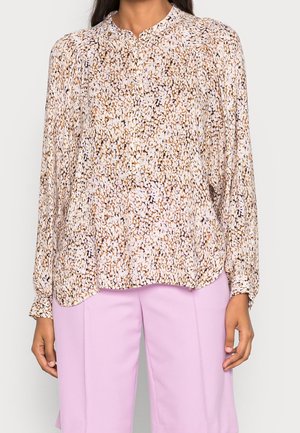 Femme portant un chemisier à manches longues avec un motif multicolore, associé à un short violet clair jusqu'aux genoux.