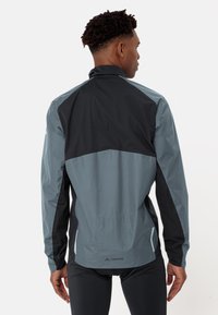 Veste légère pour homme avec un design en blocs de couleur gris et noir, fabriquée en matériau synthétique avec une texture lisse et des accents réfléchissants.