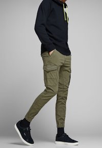 Pantaloni cargo verde oliva con molte tasche laterali, polsini elasticizzati e una vestibilità comoda, abbinati a un felpa blu navy con accenti gialli.