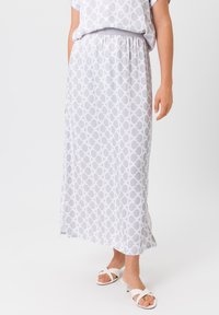 Maxi rok in lichtgrijze stof met een cirkelpatroon, elastische tailleband en zijsplits. Gepaard met witte sandalen voor contrast.