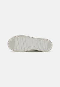 Semelle de sneaker en caoutchouc blanc avec des rainures horizontales et verticales, présentant une légère courbure vers l'avant. "Calvin Klein" embossé près du talon.