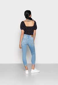 Blusa negra con estampado floral, mangas abullonadas y escote cuadrado, combinada con jeans skinny azul claro y zapatillas blancas.