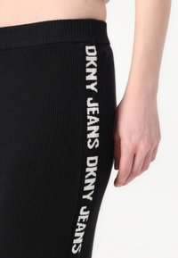 Melni jauki legingi ar baltu vertikālu logo uzdrukā "DKNY JEANS" sānos, ar elastīgu jostasvietu un gludu tekstūru.