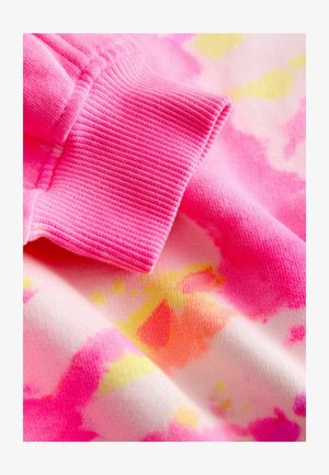 Lähivõte roosast soonikuga mansetist värvilisel lipsuvärvimise kangal, millel on roosad, kollased ja oranžid laigud.