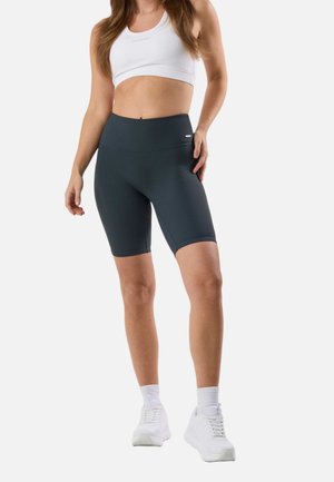 Woman wearing white sports bra, dark gray ribbed high-waist bike shorts, white crew socks, and white athletic shoes.