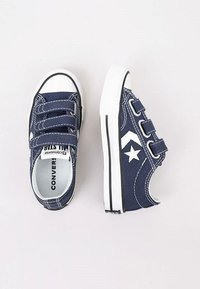 Baskets en toile bleu marine avec des bandes à velcro, bout en caoutchouc blanc et bande noire sur la semelle. Détail notable avec un logo étoile.