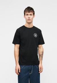 Zwarte katoenen T-shirt met korte mouwen, ronde halslijn, voorzien van een wit grafisch logo op de linkerbovenborst. Glad van structuur.