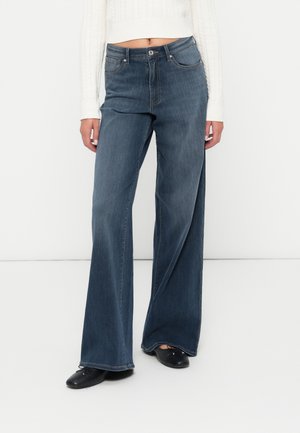 Wijduitlopende denim jeans in medium blauw. Voorzien van een klassieke vijf-pocket stijl, metalen knoopsluiting en subtiele verticale textuur.