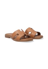 Tan leather slide sandals featuring two cut-out design elements, a flat sole, and a minimalist aesthetic. Smooth texture and low heel.
