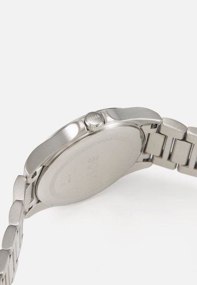 Montre en acier inoxydable avec finition brossée, boîtier rond et bracelet en maillons métalliques. Présente une couronne texturée avec la marque "BOSS".