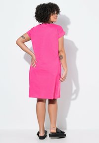 Kort rosa bomullsklänning med korta ärmar, avslappnad passform och sidoklyftor. Kombinerad med svarta skosandaler och minimala accessoarer.