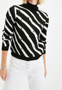 Musta-valkoraidallinen pooloneule, jossa on pitkät hihat, kohokuvioitu neulontamalli sekä resorit hihoissa ja helmassa. Yhdistetty valkoisiin housuihin.