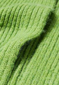 Tissu tricoté vert doux avec texture côtelée, montrant des plis et des fibres de fil détaillées.