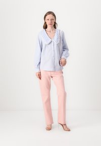Camicia a righe blu e bianche con un ampio colletto rifinito in pizzo, abbinata a pantaloni dritti rosa chiaro e tacchi nudi.