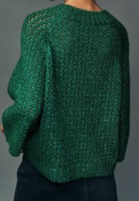 Pull en tricot vert avec une maille lâche et aérée, un col côtelé et une coupe décontractée. La texture scintillante crée un effet chatoyant.