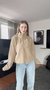 Pullover de fleece bege com colarinho alto e fecho de meio zip, apresentando uma superfície texturizada. Combinado com jeans de denim azul claro.