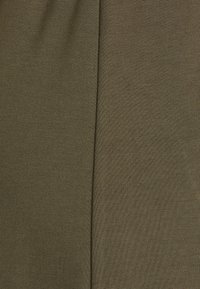 Olive zelená tkanina s textúrovaným povrchom, ktorá obsahuje vertikálny plisovaný detail. Materiál vyzerá mäkko a je mierne elastický.