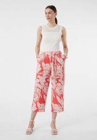 Coralfarbene Hosen mit Blumenmuster und lockerer Passform, ausgestattet mit einem Kordelzugbund und Seitentaschen, kombiniert mit einem weißen, gerippten Tanktop.