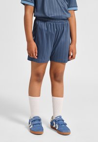 Dunkelblaue Sportshorts mit vertikalen Streifen, elastischem Bund, kombiniert mit weißen Socken und blauen Turnschuhen mit Klettverschluss und Akzenten.