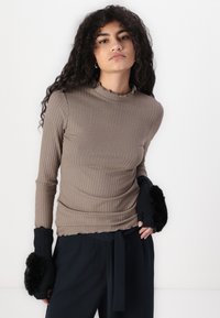 Ribbed long-sleeve top in taupe with a ruffled neckline; paired with fingerless black gloves featuring a faux fur accent. Sleek silhouette.