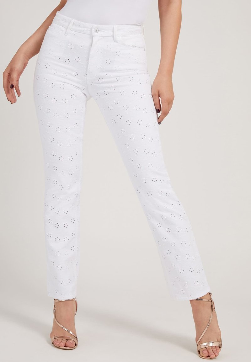 Pantaloni di cotone bianchi con design ad occhiello, vestibilità dritta, vita media e sottili motivi floreali. Abbinati a sandali metallici con cinturini.
