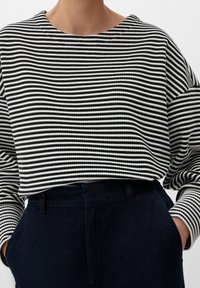 Randig tröja i svart och vitt, med en lös passform, bred halsringning och texturerad tyg, ihop med mörka denimbyxor med hög midja.