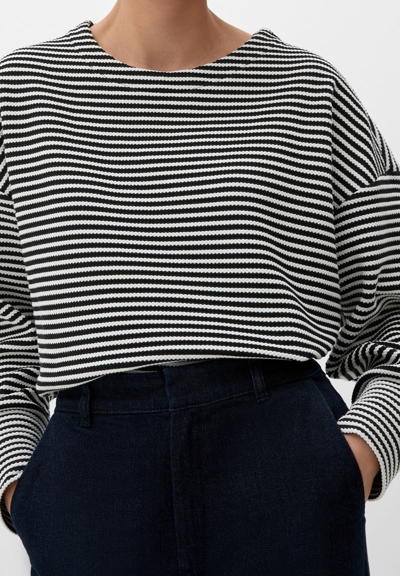 Randig tröja i svart och vitt, med en lös passform, bred halsringning och texturerad tyg, ihop med mörka denimbyxor med hög midja.