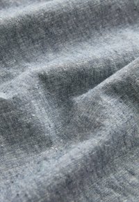 Gros plan sur un tissu en lin bleu clair avec une texture de tissage visible et des plis doux et naturels. Aucune personne ou objet présent.