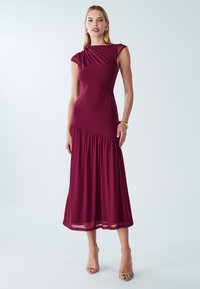 Burgundy midi-mekko, joka on valmistettu joustavasta kankaasta. Mekossa on istuva yläosa, jossa on rypytetty yksityiskohta yhdellä olkapäällä, sekä levenevä hame.