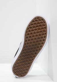 Suola della scarpa in materiale gommoso con un motivo esagonale, bordi bianchi e una presa in rilievo marrone. Piatta, con una forma ampia.