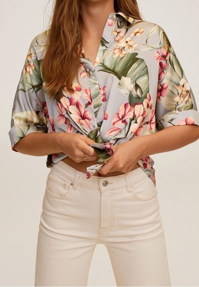 Chemise à boutons florale bleu clair avec motifs roses et verts, nouée à la taille, assortie à un jean ajusté blanc cassé.