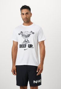 White cotton t-shirt featuring a cartoon burger lifting weights with the text "BEEF UP" and a Nike logo, paired with black shorts.