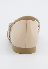 Nude kožené baleríny s kulatou zadní částí, nastavitelným řemínkem a nízkou hnědou podrážkou. Hladký povrch s pečlivými švy.