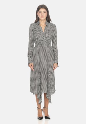 Vestito avvolgente a righe in bianco e nero con maniche lunghe e orlo arricciato, caratterizzato da una vita aderente e dettagli con bottoni. Indossato con tacchi neri.