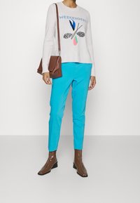 Pull rose clair avec le texte "WEEKENDERS" et un motif graphique, associé à un pantalon bleu vif et des bottines marron. Sac à bandoulière marron inclus.