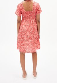 Červené šaty s vzorem, krátké rukávy, smockovaná zadní část, čtvercový výstřih a zavazování na zádech, sahající nad kolena.