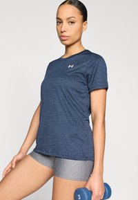 Αθλητική μπλούζα ναυτικού μπλε με κοντά μανίκια και υφή από δίχτυ, με μικρό λευκό λογότυπο· συνδυασμένη με γκρι σορτς και μπλε αλτήρα.