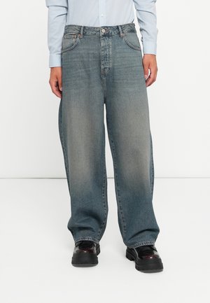 Wide-leg blue jeans with a faded wash, featuring a button and zipper closure, belt loops, and front pockets. Worn with black platform shoes.