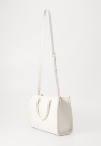 Vit handväska i texturerat läder, med dubbla handtag, ett avtagbart axelband och detaljer i guldfärgad metall.