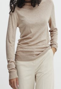 Maglione turtleneck leggero beige con maniche lunghe, polsini e orlo a costine, abbinato a pantaloni crema a vita alta. Texture morbida.