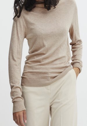 Maglione turtleneck leggero beige con maniche lunghe, polsini e orlo a costine, abbinato a pantaloni crema a vita alta. Texture morbida.